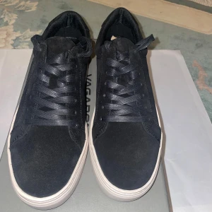 Svarta sneakers i mocka från Vagabond - Säljer ett par helt nya sneakers från Vagabond i storlek 39. Aldrig använda, bara provade hemma. Stilrena svarta skor med mjuk mocka upptill och vita platta sulor. De har klassisk snörning och rund tå, vilket ger en enkel och modern stil