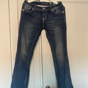 Mörkblå bootcut jeans från Miss Me - Snygga mörkblå jeans från Miss Me med bootcut passform. Jeansen har kontrastsömmar och coola bakfickor med broderade detaljer och nitar. Klassisk femficksmodell i stretchig denim som sitter skönt och ger en riktigt schysst siluett.