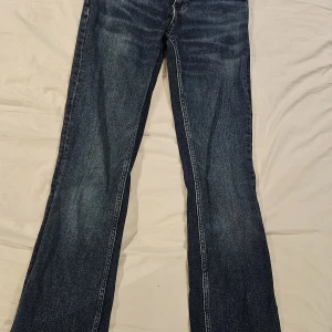 Blå bootcut jeans från MNG, strl 32 - Snygga blå jeans från MNG i klassisk bootcut-modell. Jeansen har normal passform, fem fickor och dragkedja med knapp framtill. Materialet är slitstarkt denim i bomull och färgen är mörkblå med lätt slitning för en cool look.