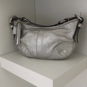Coach silver axelväska i skinn - Snygg axelväska från Coach i metallic silverfärgat skinn. Perfekt för dig som vill sticka ut med en cool accessoar. Använd fåtal ggr , säljer för 2000 kr . Köparen står för frakt. 