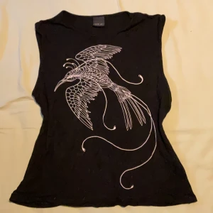 Svart ärmlös topp med fågeltryck från pta - Cool svart ärmlös topp från pta med ett stort vitt tryck av en stiliserad fågel på framsidan. Toppen har en rak passform och är perfekt för dig som gillar unika prints och vill sticka ut lite extra.