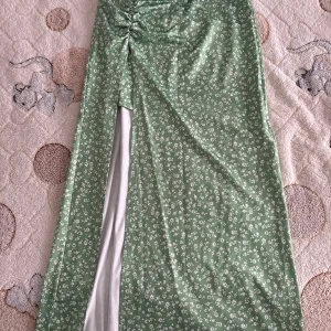 Grön blommig långkjol Shein XS - Snygg grön långklänning från Shein i storlek XS. Klänningen har små vita blommor, slits framtill med snygg rynkdetalj och är tillverkad i ett lätt, glansigt material. Perfekt för sommarens alla tillfällen!