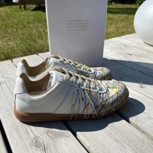 Maison Margiela sneakers med färgstänk vita - Maison Margiela färgstänk sneakers i vitt med färgstänk i blått, gult, rött och svart. Ett utmärkt val nu till sommaren. Jag har digitalt kvitto. Inga byten. Hör av vid frågor!