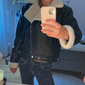 Svart jacka från Gina Tricot - Snygg svart jacka från Gina Tricot med vit fluffig krage och ärmslut. Jackan har en cool asymmetrisk dragkedja, två fickor och bältdetaljer vid midjan. Aldrig använd❣️, perfekt för dig som vill ha en varm look under höst och vinter🩵.