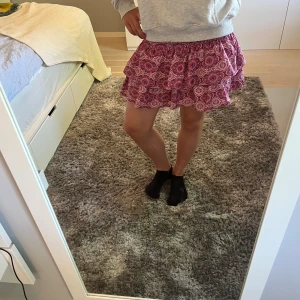 Rosa volangkjol från Meet x Tier - Supersöt kort volangkjol från Meet x Tier i rosa med blommigt mönster. Perfekt att styla med en hoodie eller en enkel topp. Nypris ca 400kr. Inga skador eller fläckar. Äkta!!