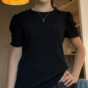 Svart strukturerad T-shirt från Vila - Supersnygg svart T-shirt från Vila med puffiga korta ärmar och coolt strukturerat tyg. Modellen är rak och har en lite loose passform, perfekt till jeans eller kjol. Tyget har en unik bubblig textur som gör att T-shirten sticker ut. Aldrig använd!! Passar mer som S/M💘🥰