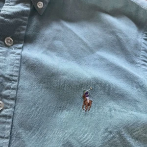 Ljusblå skjorta från Ralph Lauren - Säljer en klassisk ljusblå skjorta från Ralph Lauren med broderad logga på bröstet. Skjortan har normal passform, långa ärmar och knäppning framtill. Tillverkad i mjuk bomull, perfekt för en clean och avslappnad stil. Sitter som storlek S/XS, personen på bilden är 180!