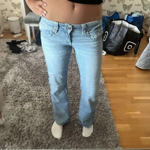 Ljusblå bootcut jeans låg midja - Säljer ett par ljusblå jeans med låg midja och bootcut-ben. Jeansen har snygga detaljer med ficklock och knappar. Super snygga💕