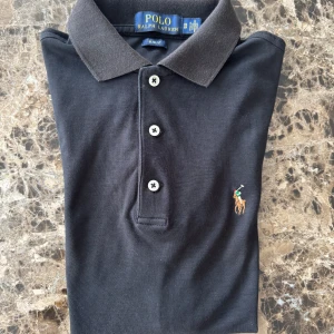 Polo Ralph Lauren Piké - En svart slimfit piké från Ralph Lauren gjord av en högt kvalitativ och exklusiv pimabomull. Skicket är i proportion med 2 års användning. Ordinariepris ligger på ca 1600kr. Digitalt kvitto från Care of Carl kan uppvisas före köp.
