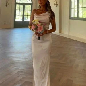 Adoore klänning - Elegant ljusrosa långklänning med smala axelband och draperad urringning. Klänningen har en figurnära passform och subtilt blommönster i tyget. Tillverkad i glansigt satinliknande material som ger en lyxig känsla. Klänningen är lite insydd i midjan hos skräddare, då jag ville ha en lång klänning tog jag en storlek större men sydde in i midjan