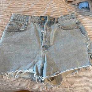 Ljusblå jeansshorts från NA-KD - Ljusblå jeansshorts från NA-KD med hög midja och råa, fransiga kanter. Bra passform