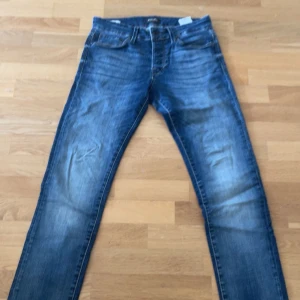 Slim fit jeans Jack & Jones Glenn - Snygga slim fit jeans från Jack & Jones, modell Glenn. De är blå med slitningar och har klassisk femficksdesign. Jeansen är i stretchigt bomullsmaterial och sitter tajt men bekvämt längs benen. Perfekta för en avslappnad och trendig look.