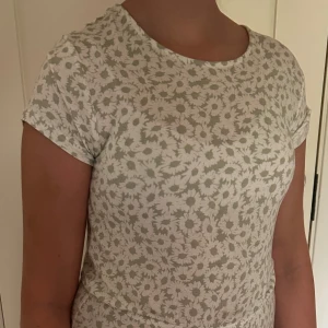 Blommig vid byxdress i grön - Superskön byxdress med ljusgrönt blommönster på vit botten. Vida ben och hög midja ger en chill och trendig look. Tillverkade i mjuk bomull, perfekta för varma dagar. Sitter löst och har en avslappnad passform.