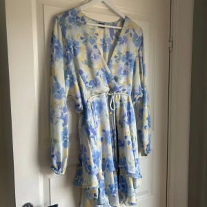 Blommig volangklänning Gina Tricot S - Superfin kort volangklänning från Gina Tricot i ljusa blå, gula och vita/grönfa ärger. Klänningen har blommigt mönster, långa ärmar med resår vid handlederna och knyt i midjan. Perfekt för vår och sommar! Endast andvänd 1 gång 😊Nypris 500 kr - klänningen finns inte längre att köpa på Gina Trico