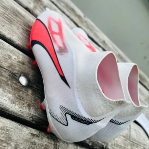 Puma ultra match, laceless FG/ AG, breakthrough, vit/ svart/fire orchid. - Puma ultra match, laceless FG/ AG, breakthrough, vit/ svart/fire orchid. Skorna har en strumpliknande passform utan snörning, mönstrad ovandel och röda dobbar för gräsplan. Lätta och snygga skor som sticker ut på planen.