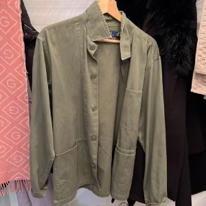 Olivgrön overshirt från Polo Ralph Lauren - Snygg olivgrön overshirt från Polo Ralph Lauren i klassisk passform. Skjortan har stora fickor framtill, knäppning hela vägen och en stilren krage. Perfekt lager-på-lager-plagg i mjuk bomull med avslappnad vibe.