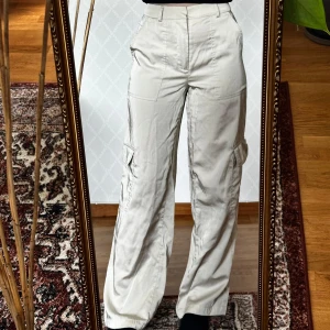 Beiga cargopants från Bik Bok - Säljer ett par beiga cargopants med hög midja från Bik Bok. Byxorna har stora fickor på sidorna och är tillverkade i ett glansigt material. Suupersköna! Men sorry för att jag inte strök byxorna innan jag fotade dem😭😂💕