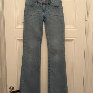 Ljusblå bootcut jeans  - Snygga ljusblå bootcut jeans med låg midja och stora framfickor. Jeansen har två bakfickor med lock och silverknappar. Tillverkade i klassiskt denimtyg. Säljer pga att de är för korta för mig i längden då jag är ca178 men verkligen så himla fina jeans!!! Köpte de för 700kr och säljer för 250kr men priset kan diskuteras. Köparn står för frakten!