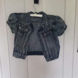Kort jeansjacka från D-XEL - Snygg kort jeansjacka från D-XEL med puffiga korta ärmar och klassiska bröstfickor. Jackan är i tvättad blå denim och har knappar framtill. Perfekt för dig som vill ha en cool och trendig look.