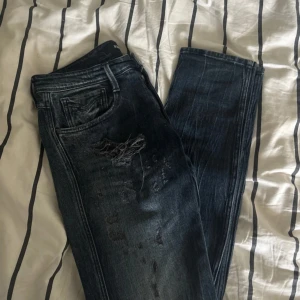 Replay Anbass slim fit jeans blå - Snygga Replay Anbass slim fit jeans i mörkblå tvätt med slitningar och trasiga detaljer på knäna. Klassisk femficksmodell med broderade bakfickor och coolt sliten look. Mycket fint skick