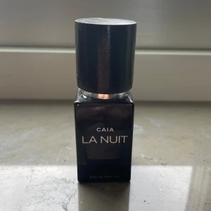 CAIA La Nuit Eau de Parfum - Snygg parfymflaska från CAIA i modellen La Nuit. Flaskan är svart och har en stilren, fyrkantig form med ett stort svart lock och silverdetalj. Texten på flaskan är i vitt och silver. Perfekt för dig som gillar exklusiva och eleganta dofter. Nästan helt full💕