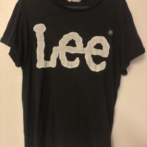 Svart Lee t-shirt med stor logga - Svart t-shirt från Lee med stor vit logga framtill. Klassisk rund hals och korta ärmar med uppvik. Skön och enkel stil som funkar till det mesta. Tillverkad i mjuk bomull för en bekväm känsla hela dagen.