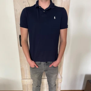 Mörkblå pikétröja från Ralph Lauren - Klassisk mörkblå pikétröja från Ralph Lauren. Storleken är M. Modellen på bilden är 179 och väger 75 kg