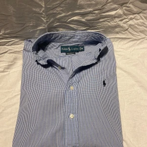 Ralph Lauren skjorta  - Klassisk blårutig skjorta från Ralph Lauren i custom fit. Skjortan har button down-krage, broderad logga på bröstet och vita knappar. Storlek M, perfekt nu för sommaren, hör av er vid frågor 
