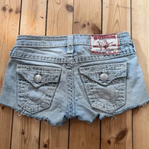 True Religion ljusblå jeansshorts - Snygga ljusblå lågmidjade jeansshorts från True Religion med råa kanter och slitna detaljer. Klassiska bakfickor med dekorativa sömmar och silverfärgade knappar. Sitter som en smäck🤗