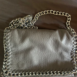 Grå axelväska med kedjedetaljer - Grå axelväska med silvrig kedja.