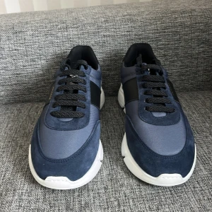 Blå sneakers från Axel Arigato - Snygga sneakers från Axel Arigato i marinblått,(helt oanvända!)och svart med vit sula. Skorna har ovandel i mocka och textil, svarta snören och en svart läderdetalj med guldfärgad logga på sidan. Bara att skriva om ni har några frågor eller prisförslag!😀