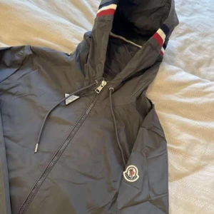 Grå vindjacka från Moncler med huva - Hej jag säljer en snygg grå vindjacka från Moncler med huva och dragkedja framtill. Denna jackan säljs åt en vän och den är i storlek 3 vilket motsvarar L om ni skulle ha några funderingar eller frågor är det bara att höra av er! Pris går att diskutera och kan mötas upp i Skåne