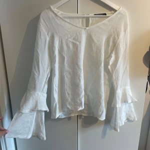 Vit blus med volangärm från Sisters Point - Superfin vit blus från Sisters Point med v-ringning och långa volangärmar. Tunt, lätt tyg i bomullskänsla och knappdetalj i nacken. Tyvärr gör liten på mig.💕den är liten i storleken och sitter som en S, inte M.