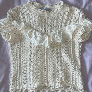 Beige stickad topp med volang från Zara - Supersöt beige stickad topp från Zara med korta ärmar och broderad volangdetalj över bröstet. Snyggt mönsterstickad med hålstickade detaljer och rund hals.💕