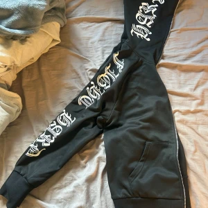 Svart hoodiejacka med tryck  - Svart hoodiejacka från SHEIN i storlek S med vita tryck längs båda ärmarna. Jackan har dragkedja framtill som går hela vägen upp till toppen, fickor och ribbade muddar. 