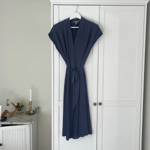 Mörkblå långklänning från H&M - Buda gärna! Säljer en stilren mörkblå långklänning från H&M i storlek 40. Klänningen har v-ringning, knytband i midjan och är ärmlös med en flowy passform. Perfekt för dig som gillar minimalistisk och clean stil. Se sista bil för litet märke, kan tvättas bort