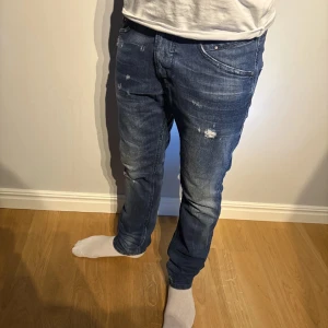 Blå Diesel jeans med slitningar - Snygga blå jeans från Diesel med coola slitningar och lätt tvättad look. Klassisk femficksmodell med raka ben och normal passform. Jeansen har detaljerade sömmar på bakfickorna och en mörk läderpatch med Diesel-logga i midjan. W27 L32. Öppen för bud