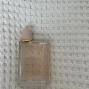 Burberry Her parfym 100ml - Burberry Her parfym i en stilren, rektangulär glasflaska med ljusrosa lock och gulddetalj. Flaskan har en lätt rosa tonad vätska och diskret ca 75% kvar