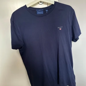 Marinblå t-shirt från Gant - Snygg marinblå t-shirt från Gant med klassisk passform och diskret logga på bröstet. Tillverkad i mjuk bomull som känns skön mot huden. Perfekt för en clean och stilren look.