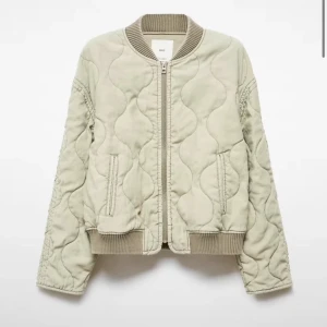 Grön quiltad bomberjacka  - Säljer en beige quiltad bomberjacka med vågigt mönster och ribbade muddar vid hals, ärmslut och nederkant. Jackan har dragkedja framtill och två fickor. Perfekt för dig som vill ha en chill och trendig look.