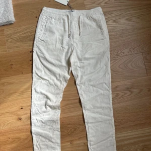 Vita linnebyxor från Solid med snörning - Snygga vita linnebyxor från Solid med prislappen har elastisk midja och snörning. Byxorna har sidfickor och bakfickor.Är regular fit och nya kostar 650