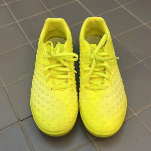 Neongula Nike fotbollsskor - Snygga neongula fotbollsskor från Nike med coolt prickigt mönster på ovandelen. Skorna har snörning och är tillverkade i syntetmaterial.