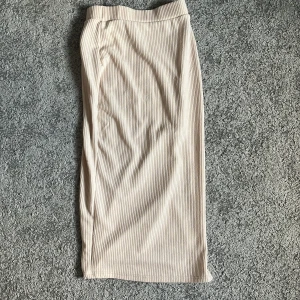 Beige ribbad långkjol med slits - Säljer en beige ribbad långkjol med snygg slits på sidan. Kjolen har en rak passform och är gjord i ett mjukt, stretchigt material som sitter skönt på kroppen. Perfekt för dig som gillar stilrena och enkla plagg med en twist.