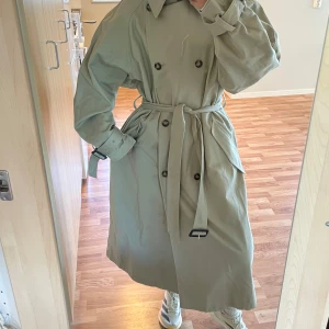 Beige trenchcoat från H&M i bomull - Snygg beige trenchcoat från H&M i storlek M. Jackan har dubbelknäppning, bälte i midjan och klassisk krage. Tillverkad i bomull med 20% återvunnet material. Perfekt oversized passform och långa ärmar med spänne vid handlederna.