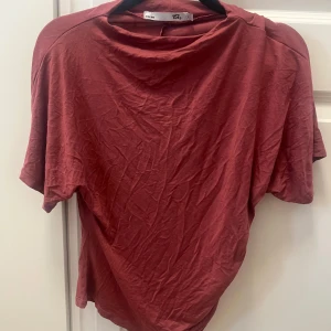 Röd t-shirt från 157 med drapering - Säljer en röd t-shirt från 157 i mjuk bomull. T-shirten har korta ärmar, lös passform och en snygg drapering på ena sidan baktill. Perfekt för dig som gillar en chill och avslappnad stil. Säljer den då den inte kommer till användning 