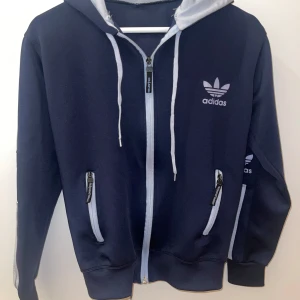 Adidas träningset  - Snygg mörkblå träningsset, dragkedja framtill. Tröjan har huva med snörning, två fickor med dragkedja och Adidas-logga på bröstet. Perfekt för en sportig och avslappnad stil. Fått som present, oklart om den är äkta.