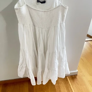 Vit somrig klänning från Zara XS - Superfin vit klänning från Zara i storlek XS. Smockad upptill med tunna axelband och volangig kjol. Lätt och luftig, perfekt för varma dagar. Tillverkad i bomull för en skön känsla. Enkel och stilren design som känns fräsch och trendig.