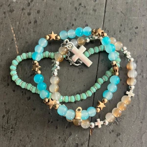 Färgglada pärlarmband med stjärnor & kors - Säljer 3 unika armband med pärlor i blått, grönt/turkos och beige💕 Ett armband har guldiga stjärnor, ett har silverfärgade kors och ett har små silver detaljer!Helt perfekt för dig som gillar att mixa och matcha smycken som passar till allt, så fint nu till sommaren!💗