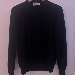 Svart kashmirtröja från Brunello Cucinelli - En stilren svart tröja från Brunello Cucinelli i lyxig kashmir. Klassisk rund halsringning och långa ärmar. Perfekt för dig som gillar en clean och tidlös look med premiumkänsla. Snyggt ribbade muddar vid ärmslut och nederkant.