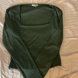 Mörkgrön långärmad topp från Amisu - Snygg mörkgrön långärmad topp från Amisu med fyrkantig urringning. Tunn och mjuk känsla, perfekt att styla med jeans eller kjol. Enkel design som ger en clean look och passar dig som gillar stilrena plagg.